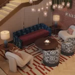 Cozy lounge area with eclectic interior design, featuring a patterned rug, a mix of plush armchairs with bold prints, a burgundy sofa, a round wooden coffee table, and ambient lighting from hanging pendant lamps, creating a warm and inviting atmosphere